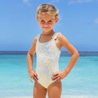 Shade Critters girls ribbed one piece swimsuit in butter blooms floral print with ruffle straps, stylish kids swimwear shown on beach.