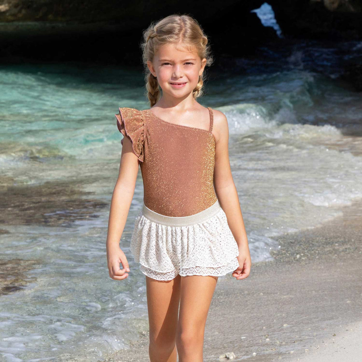 adorable kids swim photo on the beach. Shade Critters Shimmer Mocha Girls One Shoulder One Piece & Crochet Skirt Set, highlighting the metallic mocha swimsuit and soft crochet skirt with shimmery waistband.