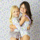 Girls wearing wildflower print one piece swimsuits with lilac fringe detail.
